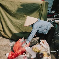 Person in conical hat collecting trash bags by Tuaans