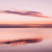 Calm water reflects a pastel sunset sky with clouds by Freddie Addery