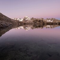 Snow-capped mountains reflected in calm lake at dusk by Christian Cueni