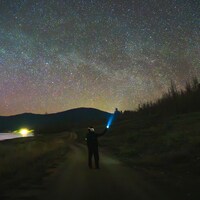 Person with flashlight under a vibrant starry night sky by Samuel Quek