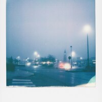 Streetlights illuminate a foggy, wet city street at night by Qinru Xie