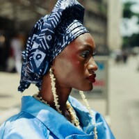 A woman in a blue headwrap and jacket with long shell earrings in Lagos by Ben Iwara