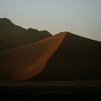 Golden sand dune against dark mountains at dusk by NIR HIMI