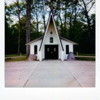 Small white chapel with a pointed roof in forest by Bruno Guerrero