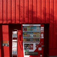 A red coca-cola vending machine against a vibrant red wall by Alexander Kaufmann