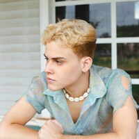 Blonde person in blue shirt and shell necklace by Bruno Dias
