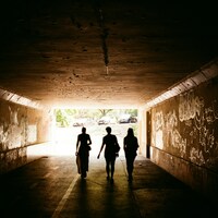 Three figures walk through a graffiti-covered tunnel by Richard Stachmann