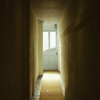 Long, dark hallway leading to a bright white door by Barney Goodman