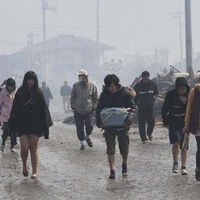 Survivors walk on a muddy street as they evacuate from tsunami-torn Natori 