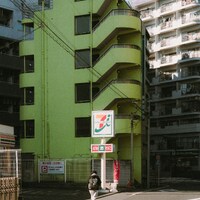 Person walks past bright green building with 7-eleven sign by Paul Yong