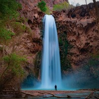 A tall waterfall cascades into a turquoise pool below by Tom Gainor