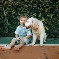 A young boy and a golden retriever puppy sit together by Helena Lopes