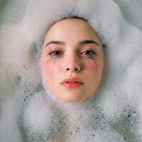 Woman's face submerged in bath bubbles by Maximus Mazar