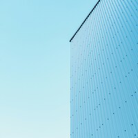 Light blue corrugated metal wall against clear sky by Andrey K