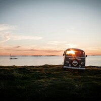 Vintage camper van parked by the ocean at sunset by Hasse Lossius