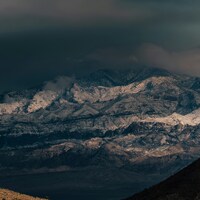 Snow-capped mountains under dark, dramatic clouds by Jonathan Ikemura