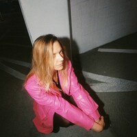 Woman in pink leather jacket crouching outdoors at night by Sasha Matveeva