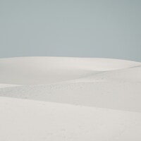 Soft white sand dunes under a pale sky by Royce Fonseca