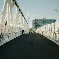 Person walks on a white pedestrian bridge covered in graffiti by Eirik Skarstein