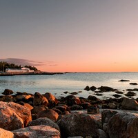 Rocky coastline at sunset with calm ocean waters by Simon Schwyter