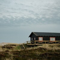Black house with red windows on a grassy dune by Max Böhme